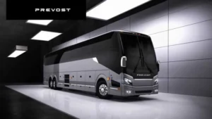 A Prevost tour bus is parked in a sleek, modern indoor showroom with dark walls and overhead lighting.