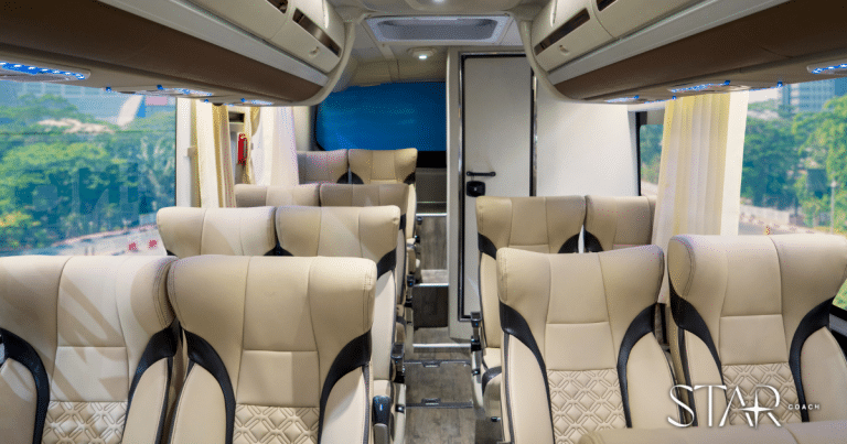 Interior of a modern coach bus with beige and black leather seats arranged in rows, overhead storage, and large windows showing a cityscape outside.