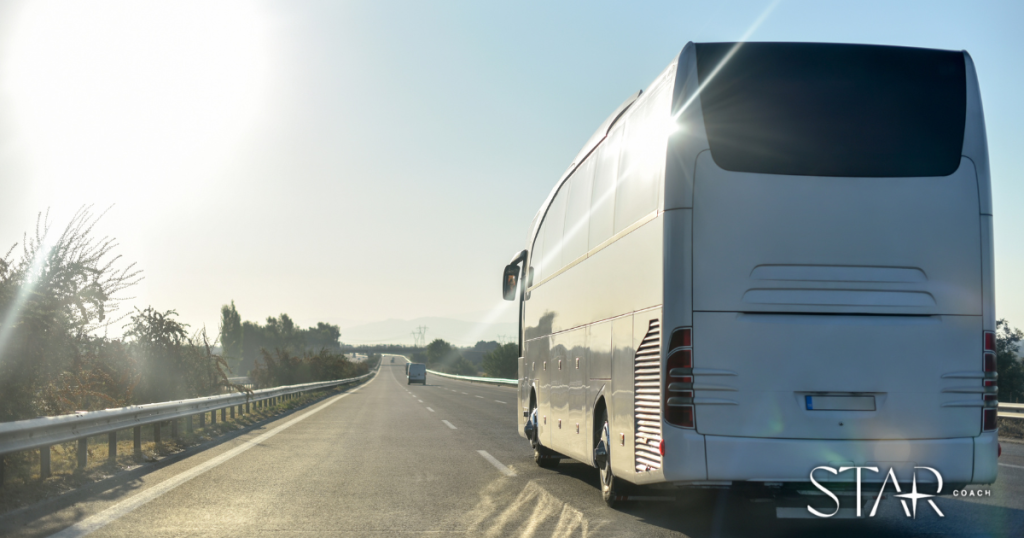 A white coach bus drives down a sunny, open highway with clear skies and minimal traffic. The STAR COACH logo is visible in the bottom right corner.