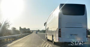 A white coach bus drives down a sunny, open highway with clear skies and minimal traffic. The STAR COACH logo is visible in the bottom right corner.