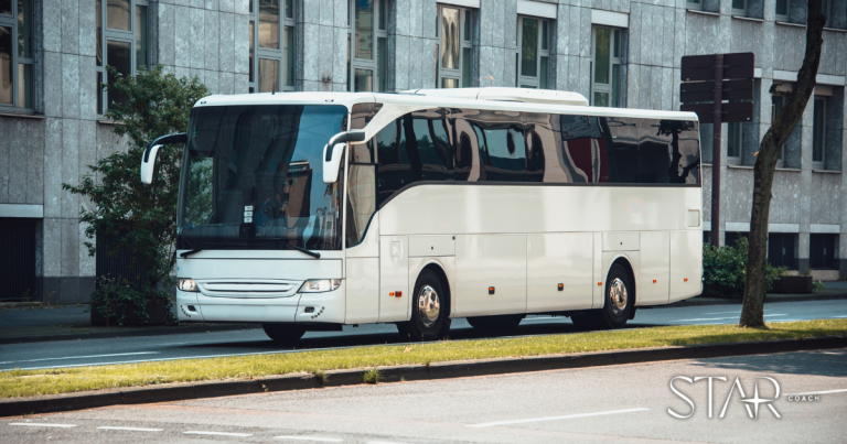 A white tour bus is parked on the side of a city street in front of a modern building with large windows. The logo "STAR Coach" is visible in the lower right corner.