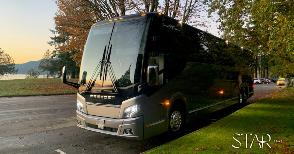 A modern black and silver Prevost tour bus is parked on a road near trees and a lake; "Star Coach" logo is visible in the lower right corner.